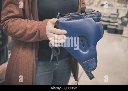 Une femme en magasin choisit d'acheter un casque bleu pour protéger sa tête pendant la boxe Banque D'Images