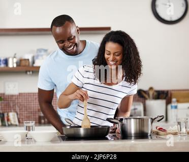 Il est tombé amoureux de sa première, puis de sa cuisine. Un jeune couple marié cuisant ensemble dans la cuisine à la maison. Banque D'Images