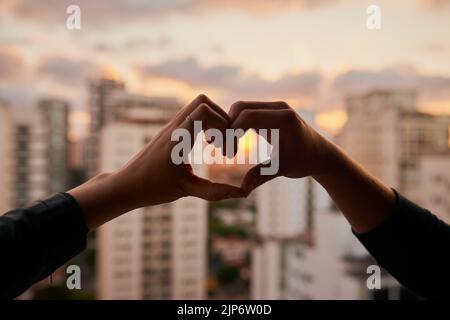 Nous adorons cette ville, un couple méconnaissable qui fait un coeur avec ses mains sur un fond de ville. Banque D'Images