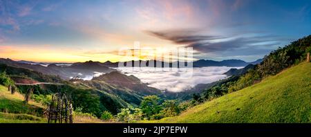 Vue panoramique sur le lever du soleil avec un sentier traversant une vallée remplie de nuages blancs dans les montagnes Tak po dans la commune de Tra Tap, dans le district de Nam Tra My Banque D'Images