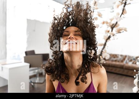 Photo avec mouvement d'une femme smiley avec des cheveux bouclés agitant les cheveux dans un salon de beauté Banque D'Images