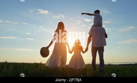 La famille heureuse aime marcher ensemble sur la prairie contre le ciel Banque D'Images