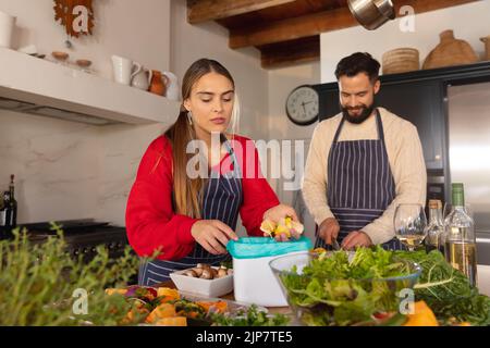 Heureux couple caucasien préparant la nourriture dans la cuisine et compostage des morceaux de légumes Banque D'Images