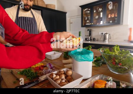 Heureux couple caucasien préparant la nourriture dans la cuisine et compostage des morceaux de légumes Banque D'Images