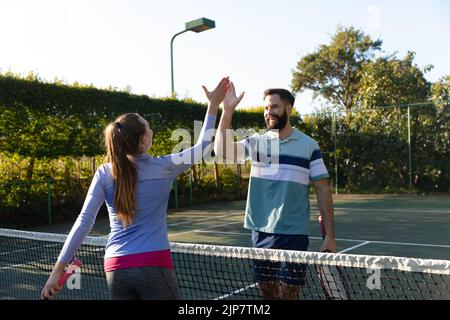Joyeux couple caucasien jouant au tennis en serrant les mains sur le filet sur le court de tennis extérieur Banque D'Images