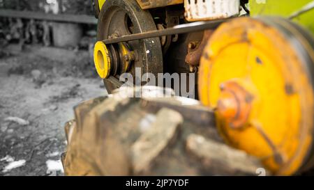 Gros plan du tracteur de jardin sur un fond noir et blanc. Poulie jaune avec entraînement par courroie pour transmission de couple. Roue à large bande de roulement Banque D'Images