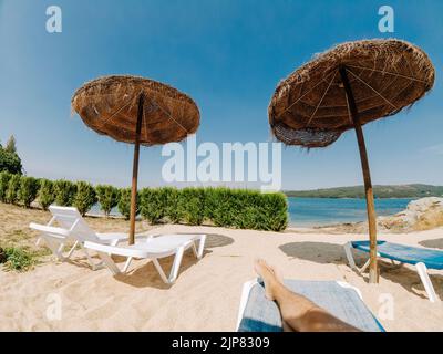 Point de vue d'un touriste sur des chaises longues avec des parasols en paille près de la rivière avec des plantes Banque D'Images