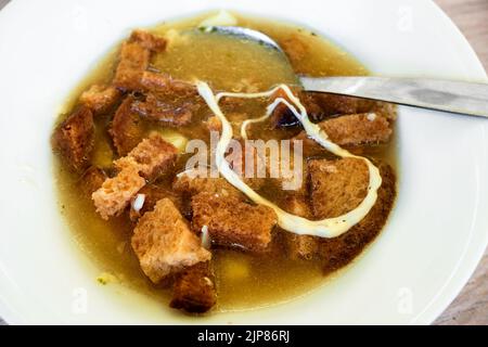 Soupe à l'ail avec pain poêlé en tranches et fromage fondu, cuillère dans une assiette blanche, gros plan. Cuisine traditionnelle de la république tchèque. Banque D'Images