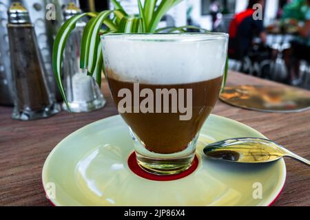 Boisson cappuccino dans une tasse de verre sur table dans le restaurant extérieur, en gros plan. Banque D'Images