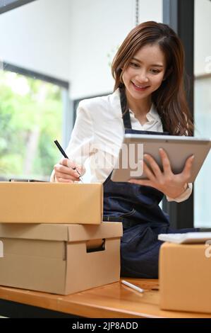 Magnifique jeune asiatique femme en ligne propriétaire de magasin en vérifiant ses paquets d'expédition dans son stock et la chambre de paquet. Banque D'Images