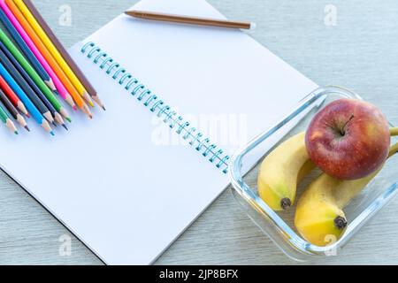 Un déjeuner sain dans un contenant en verre, un carnet vide ouvert, des crayons, des fournitures scolaires, une copie de l'espace, vue du dessus. Des repas sains à l'école. Un sna Banque D'Images