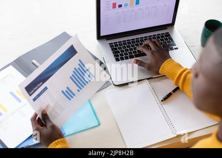 Vue d'ensemble de l'homme afro-américain utilisant un ordinateur portable et regardant des feuilles de calcul Banque D'Images