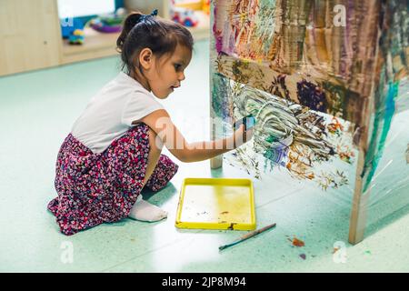 Peinture de film adhésif. Petite fille enfant peinture avec une éponge et peint sur un film adhésif enroulé tout autour de l'étagère en bois. Activité créative pour le développement des enfants à l'école maternelle. Photo de haute qualité Banque D'Images