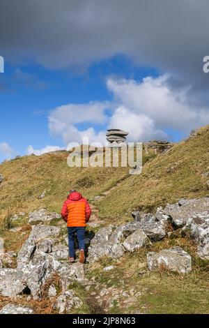 Un marcheur dans une veste rouge vif marchant sur un sentier accidenté jusqu'à la pile de rochers Cheesewring sur Stowe Hill sur Bodmin Moor dans Cornwall. Banque D'Images