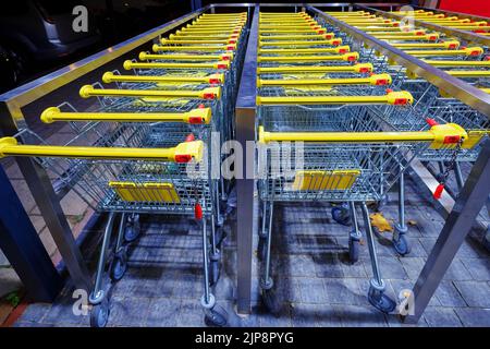 Rangée de chariots à provisions en métal empilés avec poignées jaunes près du supermarché Banque D'Images