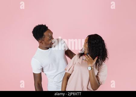 Jeune couple africain souriant deux amis famille homme femme dans des vêtements décontractés regarder les uns les autres jouer deviner qui ou cacher et chercher ensemble isolé sur couleur rose fond portrait de studio. Banque D'Images