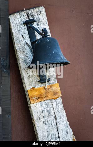 Une ancienne cloche en fer noir attachée à une planche en bois rustique avec une corde pour sonner et un signe usé en dessous en toute saison en Pennsylvanie Banque D'Images