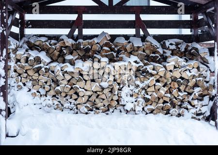 Des bûches recouvertes de neige empilées sous une verrière par une journée d'hiver Banque D'Images