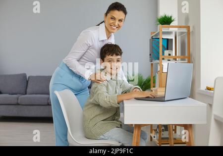 Parent heureux ou enseignant d'école aider le garçon étudiant pendant qu'il utilise un ordinateur portable Banque D'Images