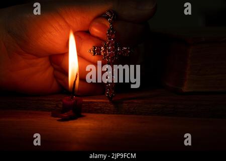 Une femme tient une croix près d'une bougie et d'une bible dans l'obscurité, une femme prie, priant, foi et religion, temple Banque D'Images