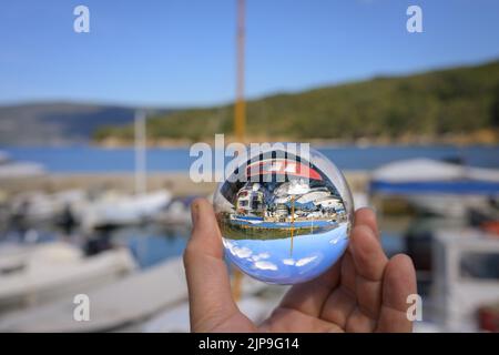 Main tenant la sphère de verre dans le petit port de Valun (Cres, Croatie), jour ensoleillé au printemps Banque D'Images