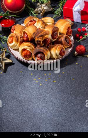 Recette traditionnelle de plat de Noël Pigs en couvertures, saucisses enveloppées dans le bacon, pâtisserie feuilletée au four hot dogs rouleaux avec des branches d'arbre de Noël, décorati Banque D'Images