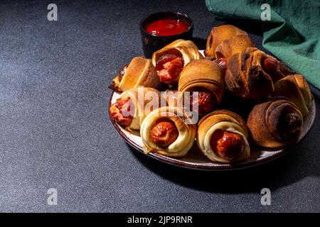 Recette traditionnelle de plat de Noël Pigs en couvertures, saucisses enveloppées dans le bacon, pâtisserie feuilletée au four hot dogs rouleaux avec des branches d'arbre de Noël, décorati Banque D'Images