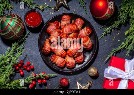 Recette traditionnelle de plat de Noël Pigs en couvertures, saucisses enveloppées dans le bacon, pâtisserie feuilletée au four hot dogs rouleaux avec des branches d'arbre de Noël, décorati Banque D'Images