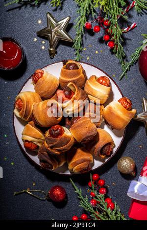 Recette traditionnelle de plat de Noël Pigs en couvertures, saucisses enveloppées dans le bacon, pâtisserie feuilletée au four hot dogs rouleaux avec des branches d'arbre de Noël, décorati Banque D'Images