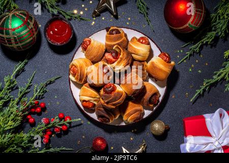 Recette traditionnelle de plat de Noël Pigs en couvertures, saucisses enveloppées dans le bacon, pâtisserie feuilletée au four hot dogs rouleaux avec des branches d'arbre de Noël, décorati Banque D'Images