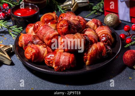 Recette traditionnelle de plat de Noël Pigs en couvertures, saucisses enveloppées dans le bacon, pâtisserie feuilletée au four hot dogs rouleaux avec des branches d'arbre de Noël, décorati Banque D'Images