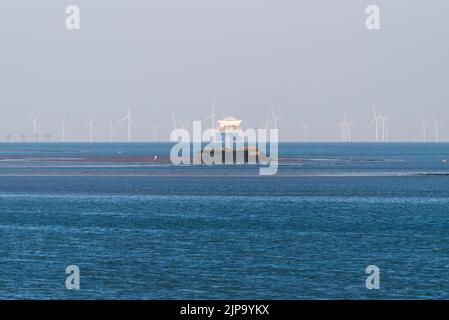 Des navires de cargaison éloignés naviguant à travers les parcs éoliens offshore de l'estuaire de la Tamise, avec des randonneurs loin de la rive à la section de Mulberry Harbour au large de Southend Banque D'Images