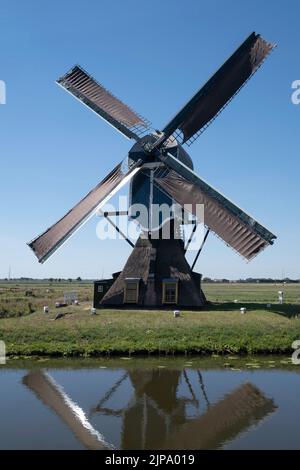 Moulin POLDER 'de Blauwe WIP' à Hazerswoude-Dorp, dans le sud de la Hollande, construit en 1636, avec de vieilles granges et réflexion dans l'eau. Soleil et ciel bleu Banque D'Images