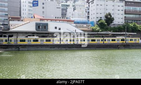 La gare JR Ichigaya est située le long d'une rivière avec le train jaune de la ligne de métro Toei-Shinjuku par une journée d'été nuageux. Banque D'Images