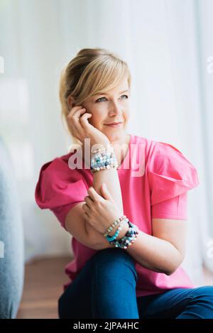 Portrait de la belle femme blonde aux cheveux assis près de la fenêtre et rêvant de jour. Banque D'Images