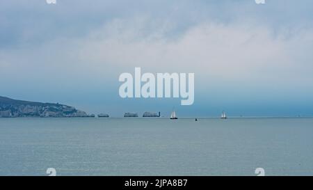 Milford-on-Sea, Hampshire, Royaume-Uni, 16th août 2022, Météo. Des averses lourdes accompagnent les nuages sombres comme la pluie nécessaire tombe sur sec, parché sud de l'Angleterre. Des voiliers blancs passent devant le phare de Needles sur l'île de Wight. Crédit : Paul Biggins/Alamy Live News Banque D'Images