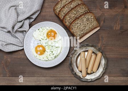 Assiette avec œufs frits, pain et susages sur une table en bois. Heure du petit déjeuner Banque D'Images