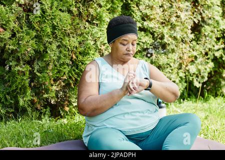 Portrait d'une femme noire mûre regardant la montre intelligente tout en prenant une pause dans l'entraînement en plein air Banque D'Images