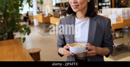 Jeune femme portant un costume tenant une tasse de café debout dans un café. Banque D'Images