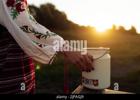 La femme ukrainienne se tient dans une chemise et une jupe nationales brodées traditionnelles et tient le laitan sur la prairie au coucher du soleil. Vêtements nationaux ethniques ukrainiens s Banque D'Images