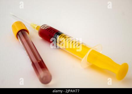 Une seringue jaune avec du sang et un tube de test sanguin à capuchon jaune, isolé sur fond blanc Banque D'Images