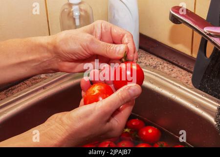 Les mains de la femme lavez les tomates et retirez les tiges des légumes. Banque D'Images