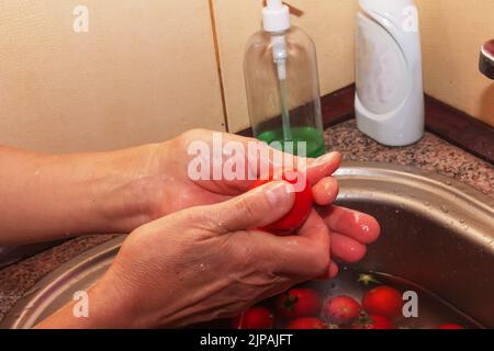 Les mains de la femme lavez les tomates et retirez les tiges des légumes. Banque D'Images