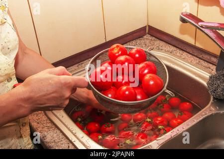 Les mains de la femme lavez les tomates et retirez les tiges des légumes. Banque D'Images