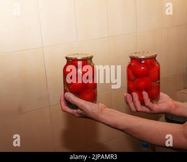 Le processus de conservation des tomates pour l'hiver. Les mains des femmes tiennent des pots avec des tomates mûres, juteuses et marinées. Banque D'Images