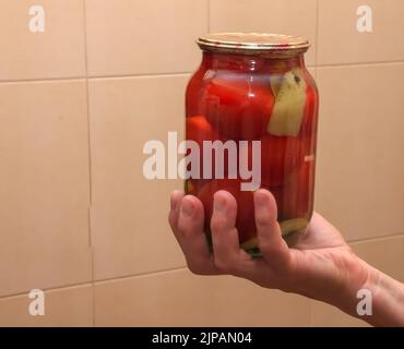 Le processus de conservation des tomates pour l'hiver. Les mains des femmes tiennent des pots avec des tomates mûres, juteuses et marinées. Banque D'Images