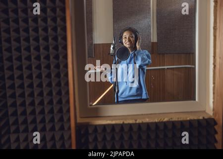 Chanteur africain adolescent portant des écouteurs, chante dans le microphone, travaillant dans un studio vocal avec plaisir et bonheur Banque D'Images