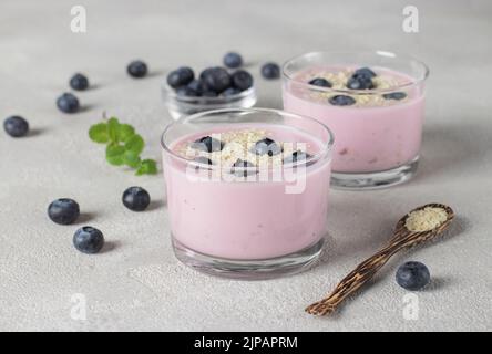 Yaourt aux bleuets et aux graines de sésame dans des verres, ainsi que dans une cuillère en bois sur fond gris Banque D'Images