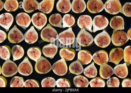 De nombreuses figues vertes fraîchement coupées se trouvent les unes à côté des autres, devant un arrière-plan sombre. Ils sont photographiés d'en haut. Banque D'Images