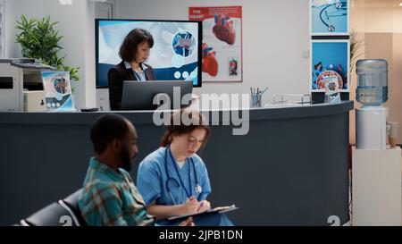 Divers groupes de patients demandant de l'aide à la réception de l'hôpital, assis dans le hall de l'aire d'attente. Mère avec enfant, homme âgé et patient asiatique ayant rendez-vous à une clinique médicale très fréquentée. Banque D'Images